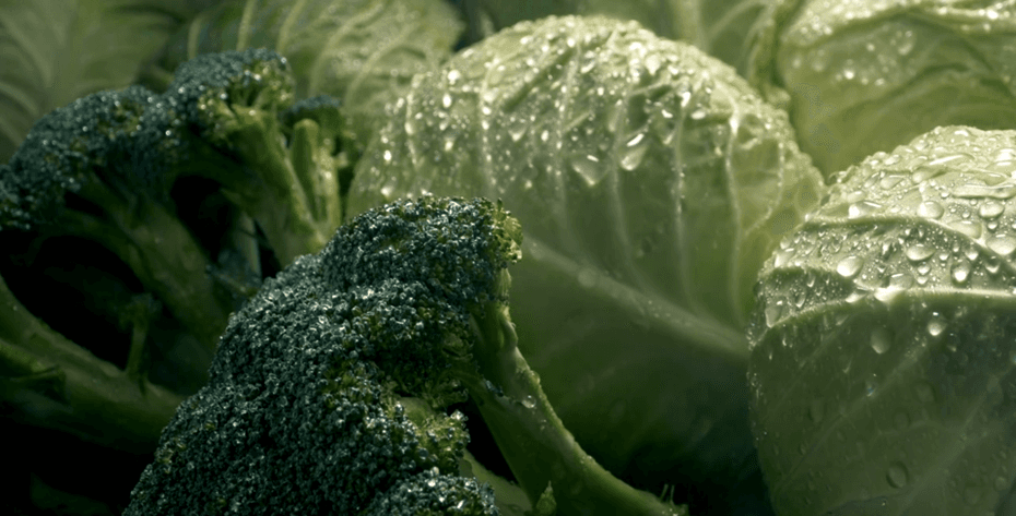Close-up of fresh green broccoli florets and cabbage leaves with water droplets.