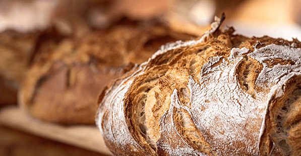 Close-up of crusty, flour-dusted artisanal bread loaves on a wooden board, with crackled golden-brown crusts and rustic texture.