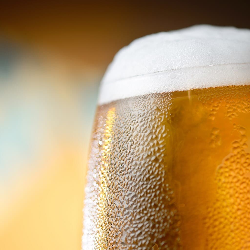 Close-up of a beer glass with a thick white head and condensation on the outside, amber liquid visible through the glass.
