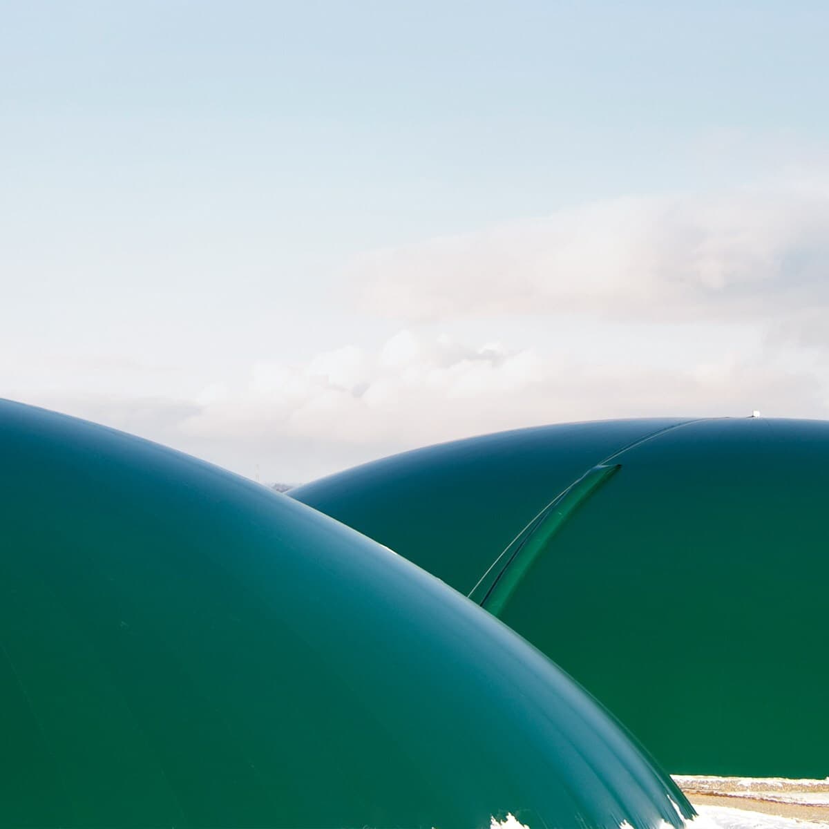 Close-up of two large, glossy green curved domes with a seam between them, set against a pale blue sky with fluffy white clouds.