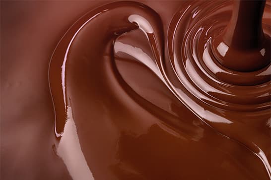 Close-up of glossy melted chocolate swirling in rich brown tones with bright highlights.