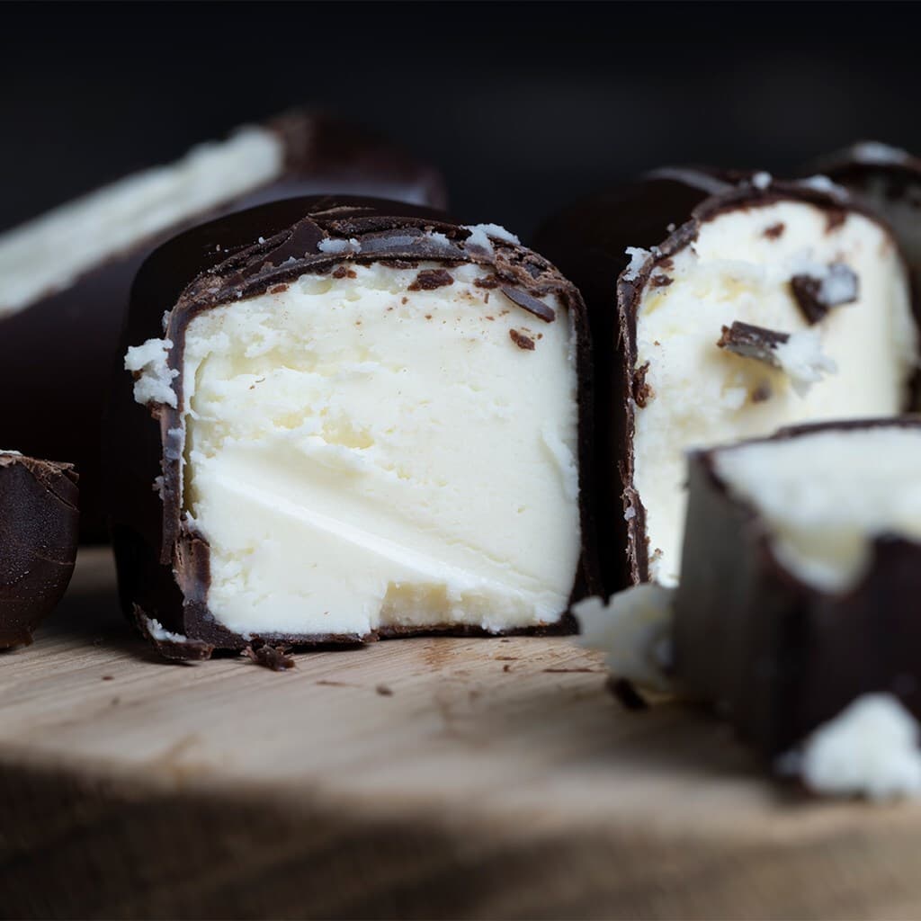 Close-up of dark chocolate-coated truffles sliced in half, exposing pale creamy centers with coconut flakes on a wooden board.