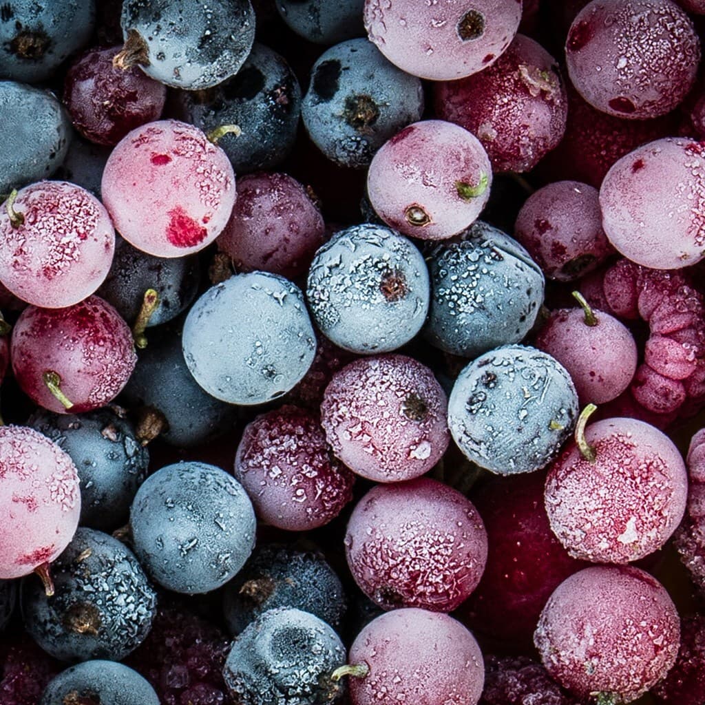 Close-up of frost-covered berries in blue, pink, and purple tones with delicate ice crystals on their skins.