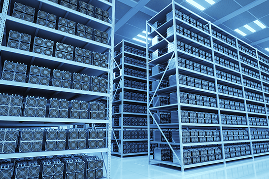 Blue-toned data center with tall metal racks filled with server units, arranged in long aisles under bright overhead lights.