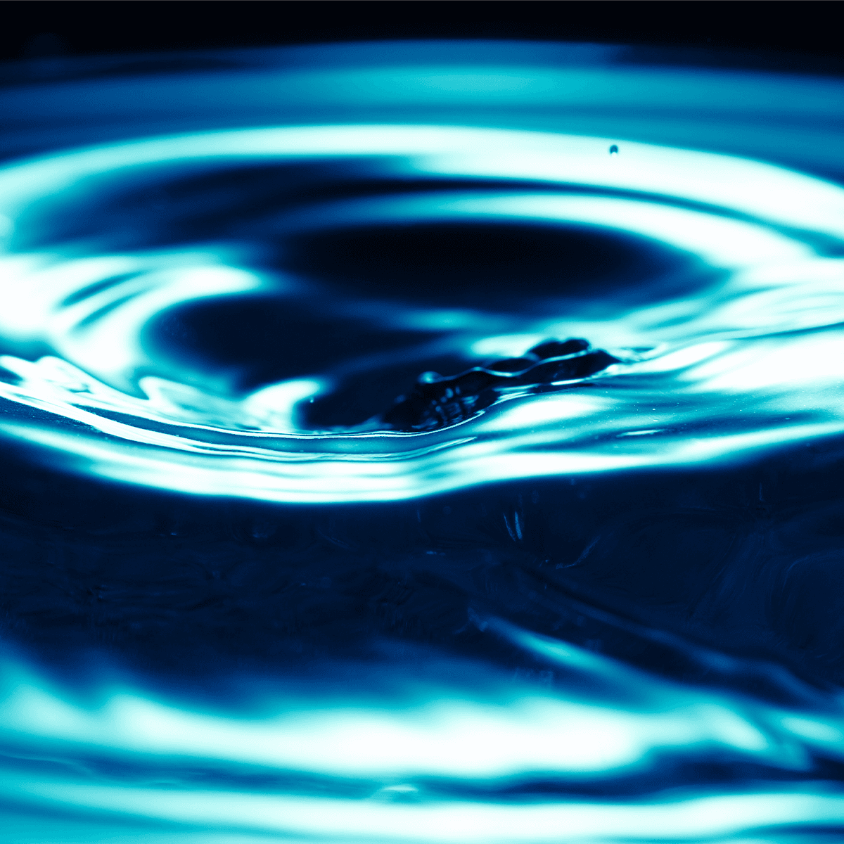 Close-up of blue liquid with glowing cyan ripples and a dark center, resembling a water ripple pattern.