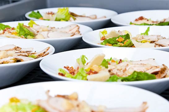 White bowls of mixed salad with greens, sliced meat, and vegetables arranged on a table.