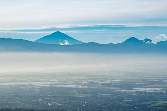 Distant blue mountains loom over a hazy valley with light fog, under a pale blue sky and wispy clouds.