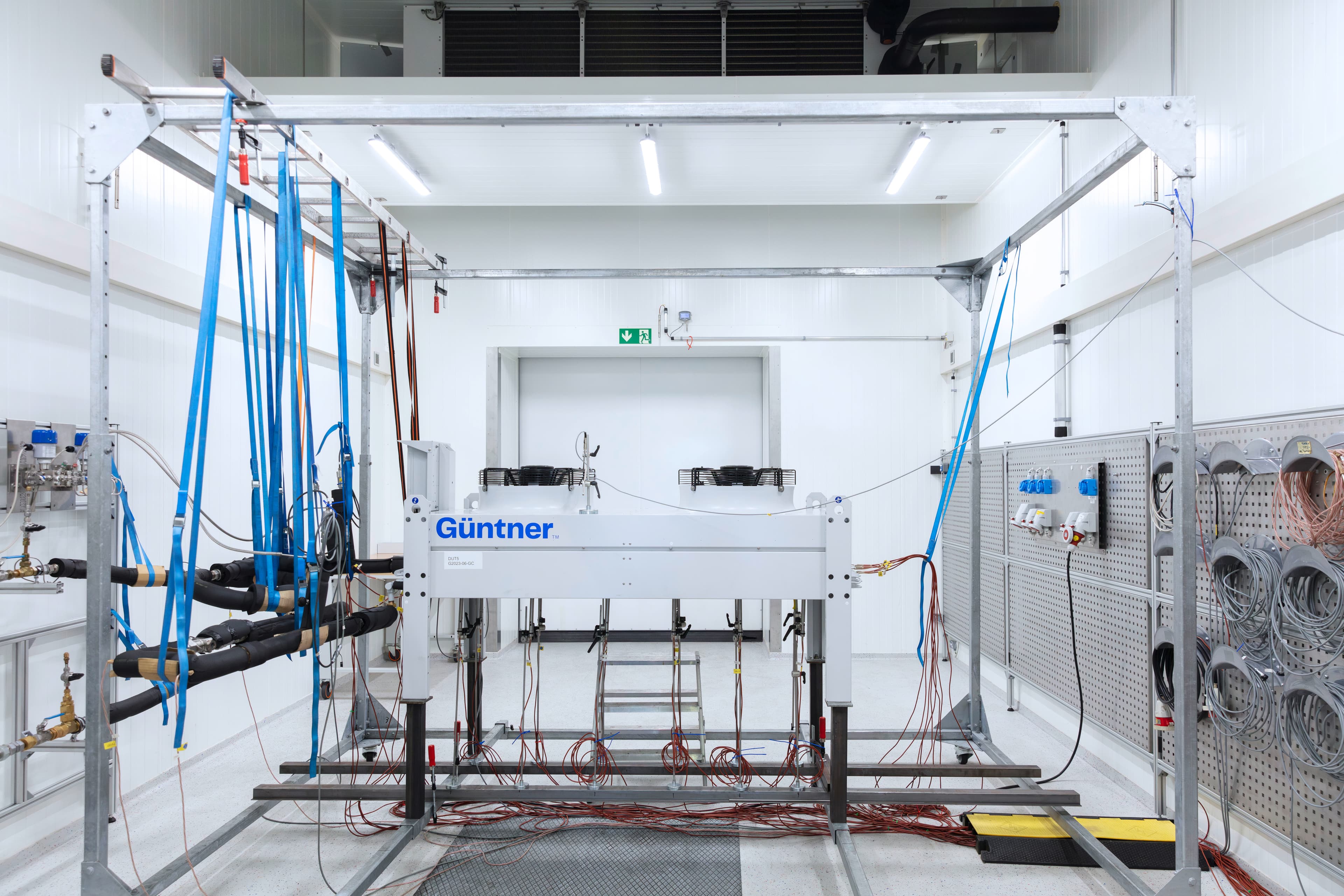 Industrial test rig in a white lab; metal frame with blue straps, hoses and cables; a Günther unit at center.