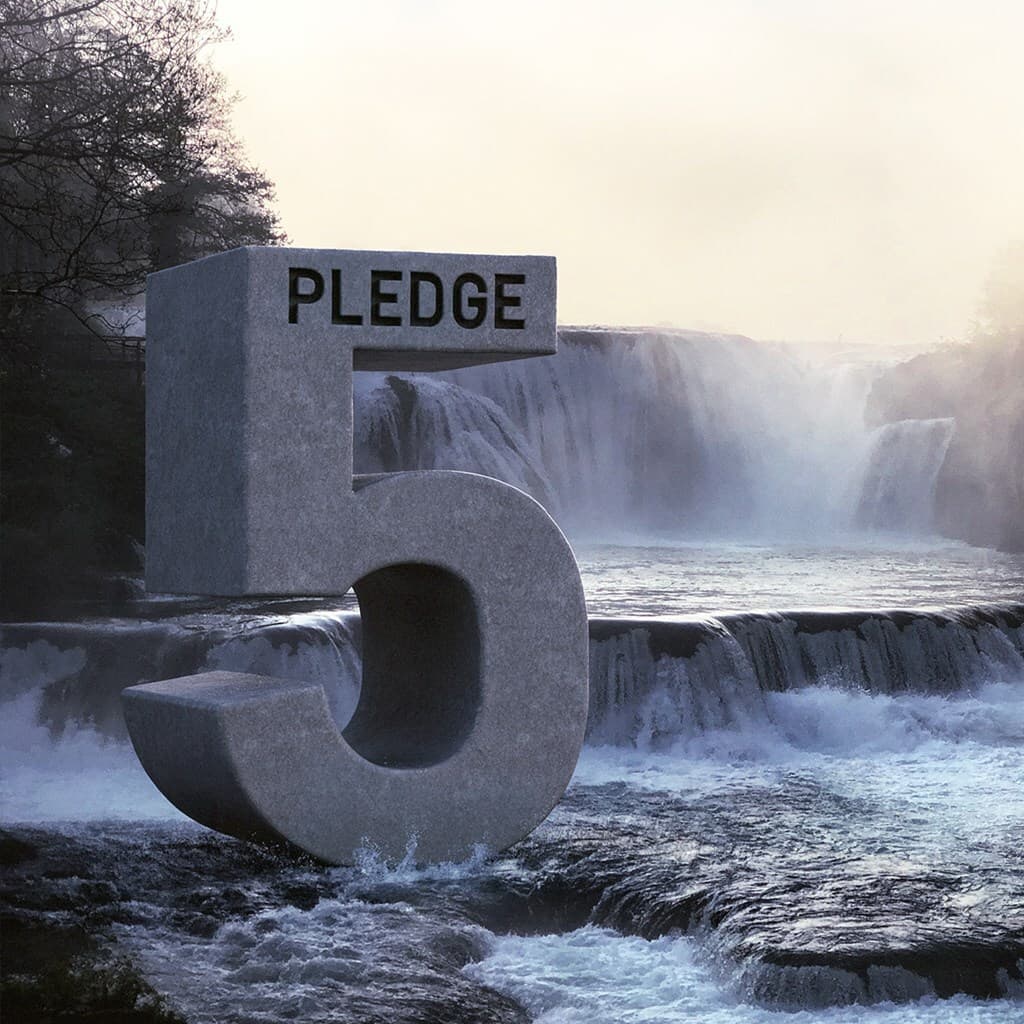 A large gray stone sculpture of the number 5 with “PLEDGE” on the top bar, set beside a wide cascading waterfall and misty river.