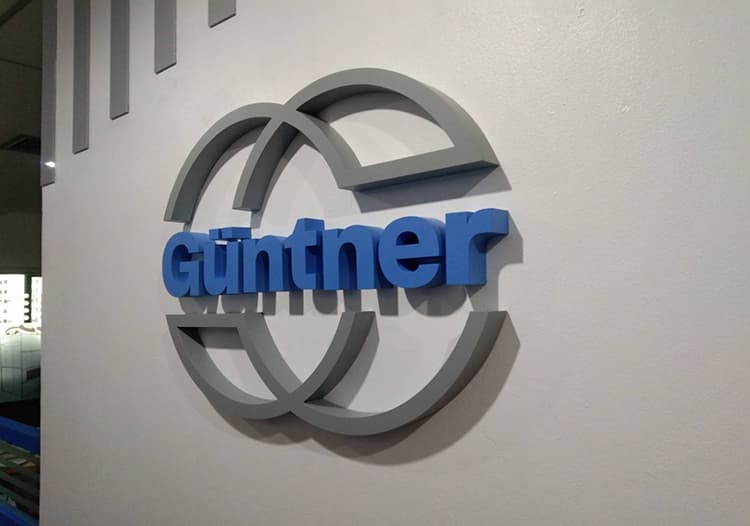 Three-dimensional blue "Günther" logo on a white wall, featuring overlapping gray circular rings around the text.