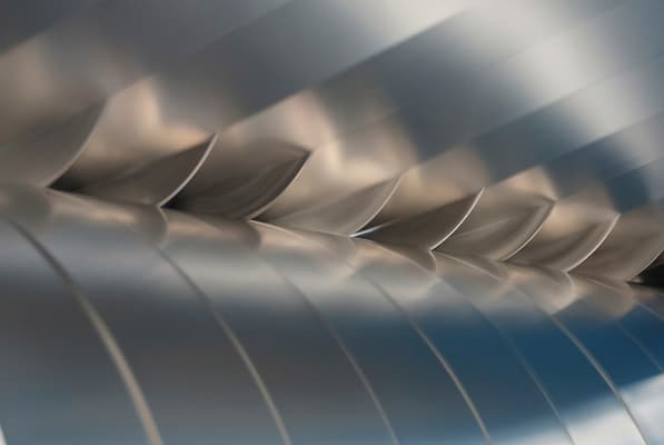 Close-up of shiny curved metal fins arranged diagonally, creating a scale-like pattern with a blurred blue background.