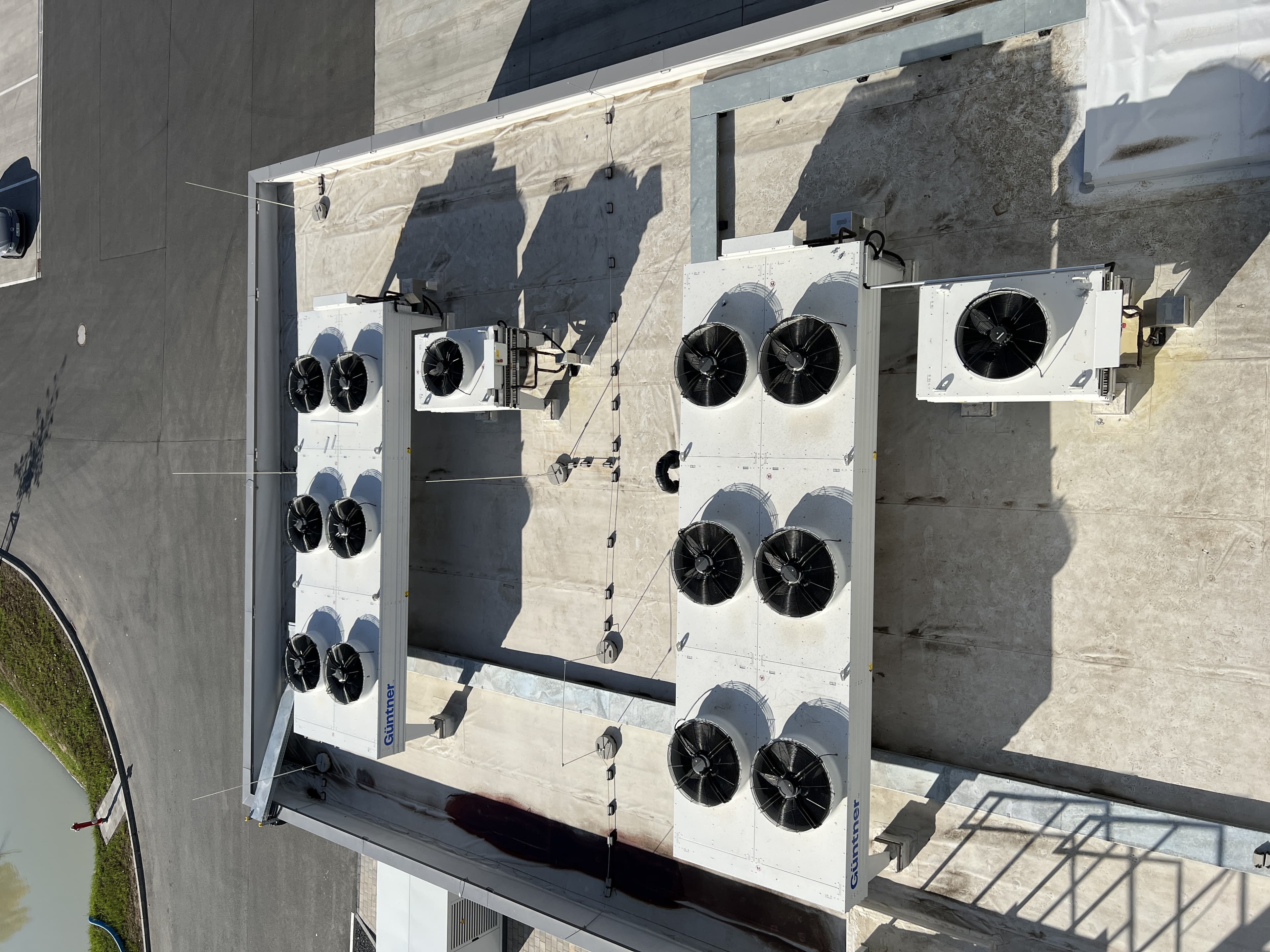 Vista aérea de azotea con varias unidades de climatización blancas y ventiladores circulares; sombras largas sobre el techo de concreto.