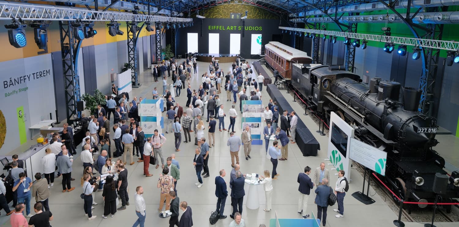 Busy indoor expo with crowds around booths; a vintage steam locomotive on the right and a stage reading Eiffel Art Studios at the far end.