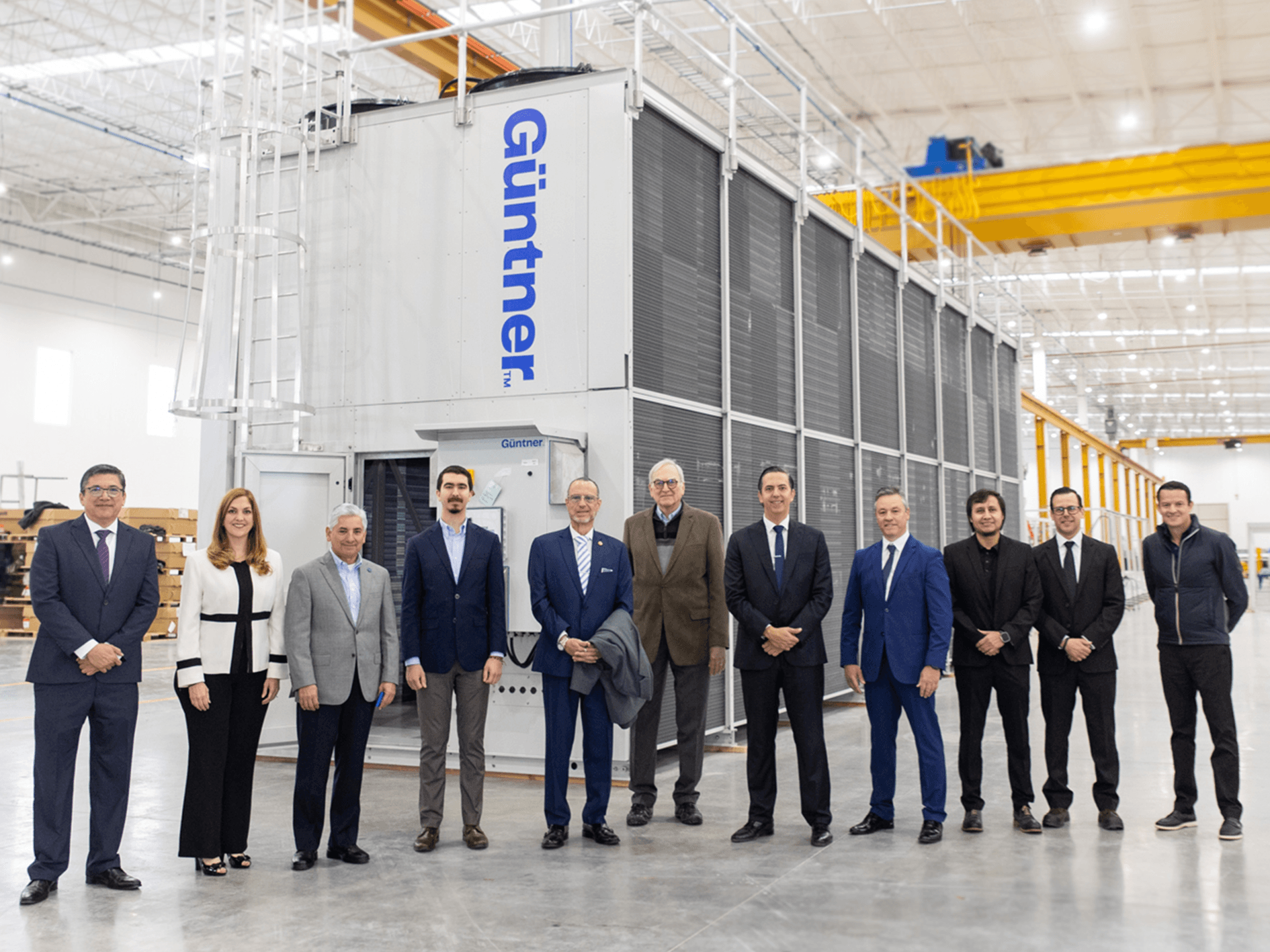 Group of professionals in business attire standing in a bright industrial facility beside a large Güntner cooling unit.