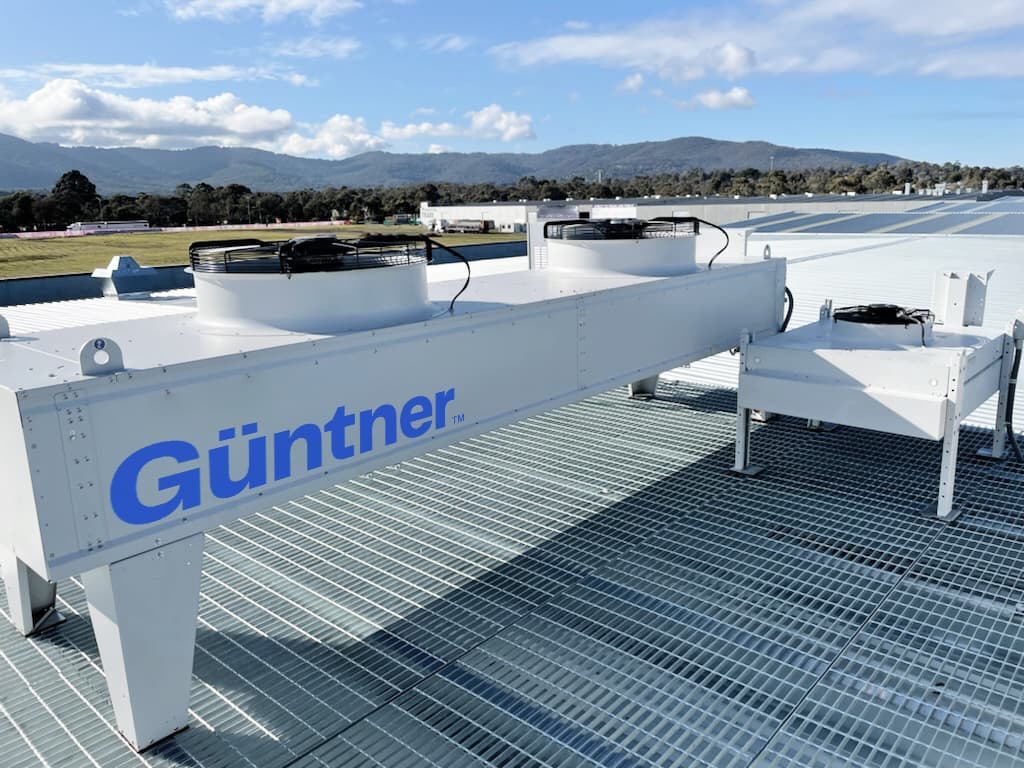 Rooftop HVAC units with large fans on a metal grate, a blue Günther logo, and a clear sky with distant mountains.