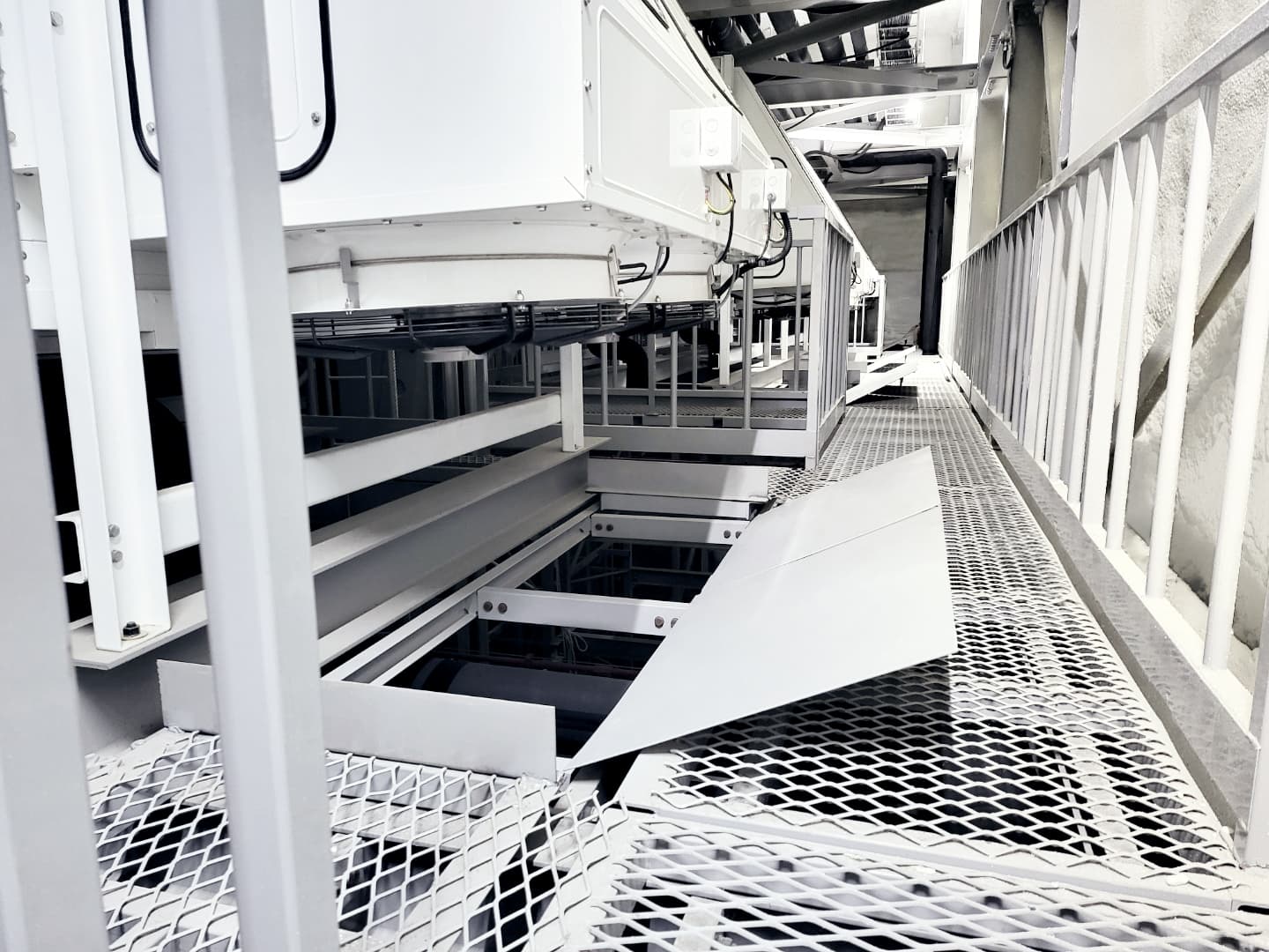 Maschinenraum mit Stahlkonstruktionen, Rohrleitungen und Metallgitterboden; white/hellgraue industrielle Anlage, Perspektive längs einer Plattform.