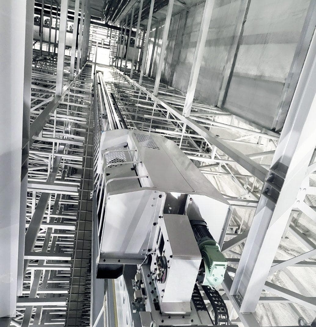 Schwerer Industriemotor und Gleistransport in einer Hochregal- oder Förderanlage aus Stahl, Blick nach oben durch metalldrahtige Konstruktionen und Kabel.