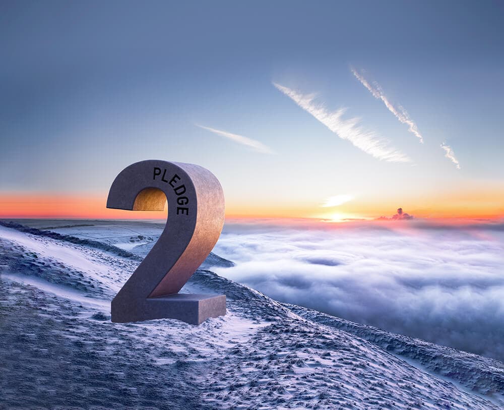Large curved numeral 2 with PLEDGE along its inner curve sits on a snow-covered mountain ridge above a sea of clouds at sunrise.