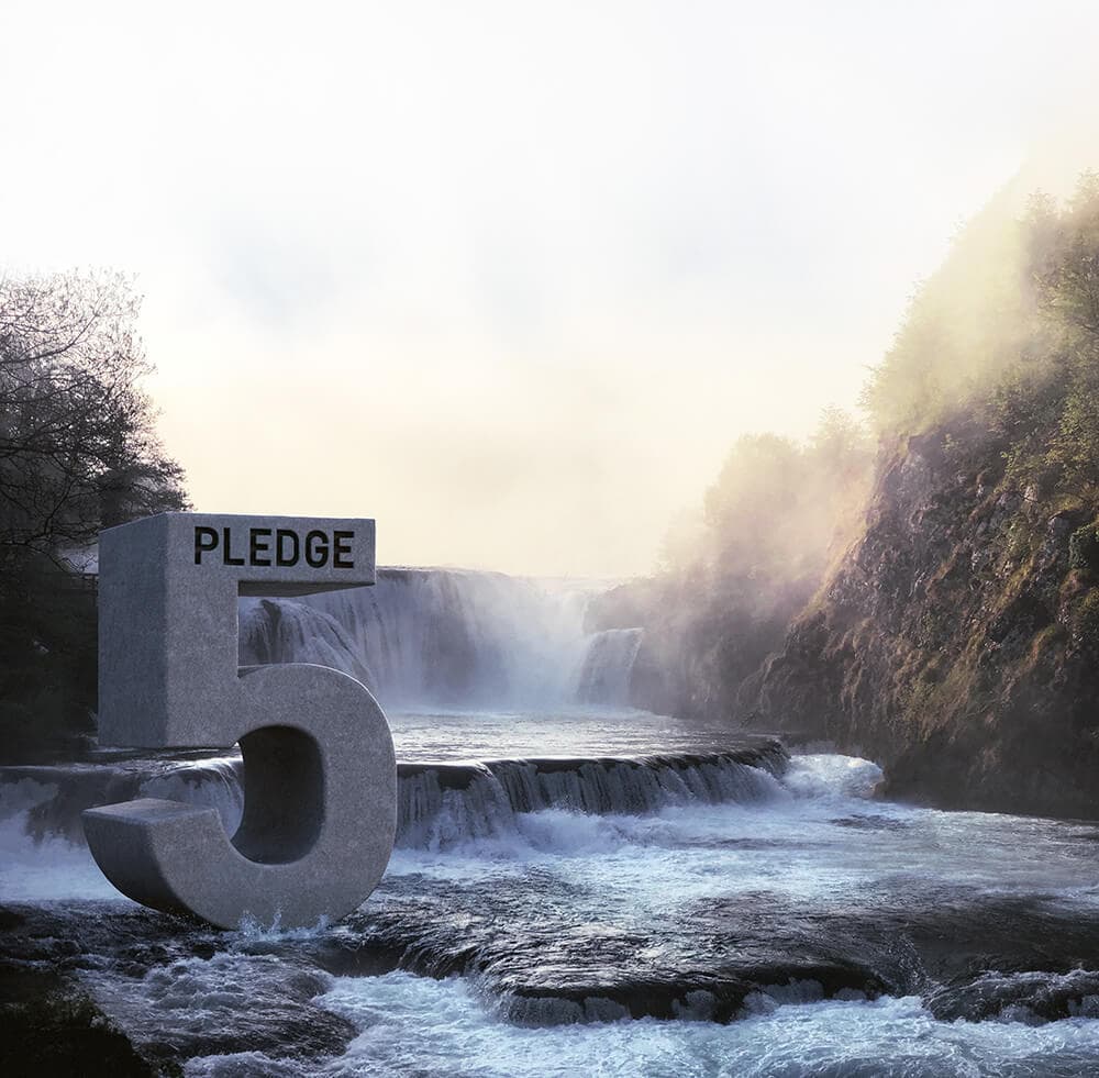 A large gray stone sculpture of the number 5 with the word PLEDGE sits in a river beside a misty waterfall and rocky cliff.