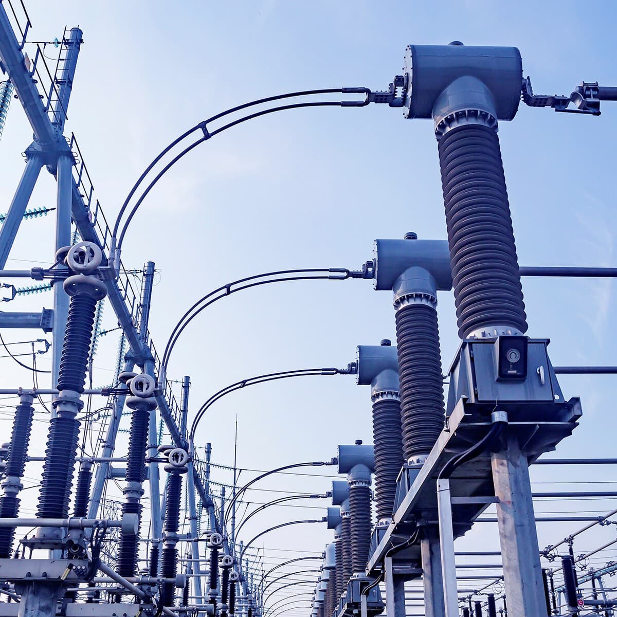High-voltage electrical substation with tall ribbed insulators, metal structures, and curved conductors against a clear blue sky.