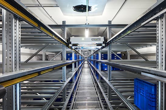Symmetrical warehouse aisle with metal storage racks, blue plastic crates on both sides, and a central metal walkway.