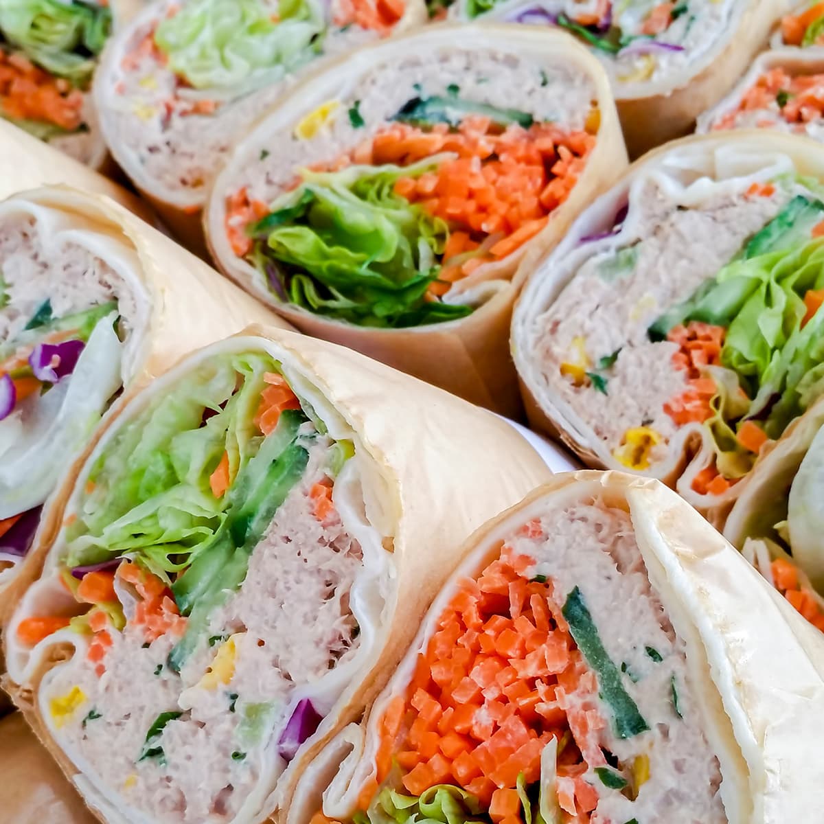 Assorted tortilla wraps cut in half, revealing lettuce, diced carrots, cucumber, purple cabbage, and a creamy filling.