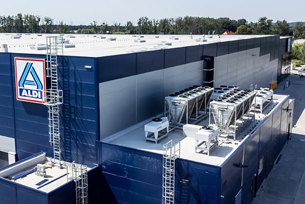 Aldi warehouse with blue exterior panels, rooftop HVAC units and ductwork, and a metal ladder along the side.