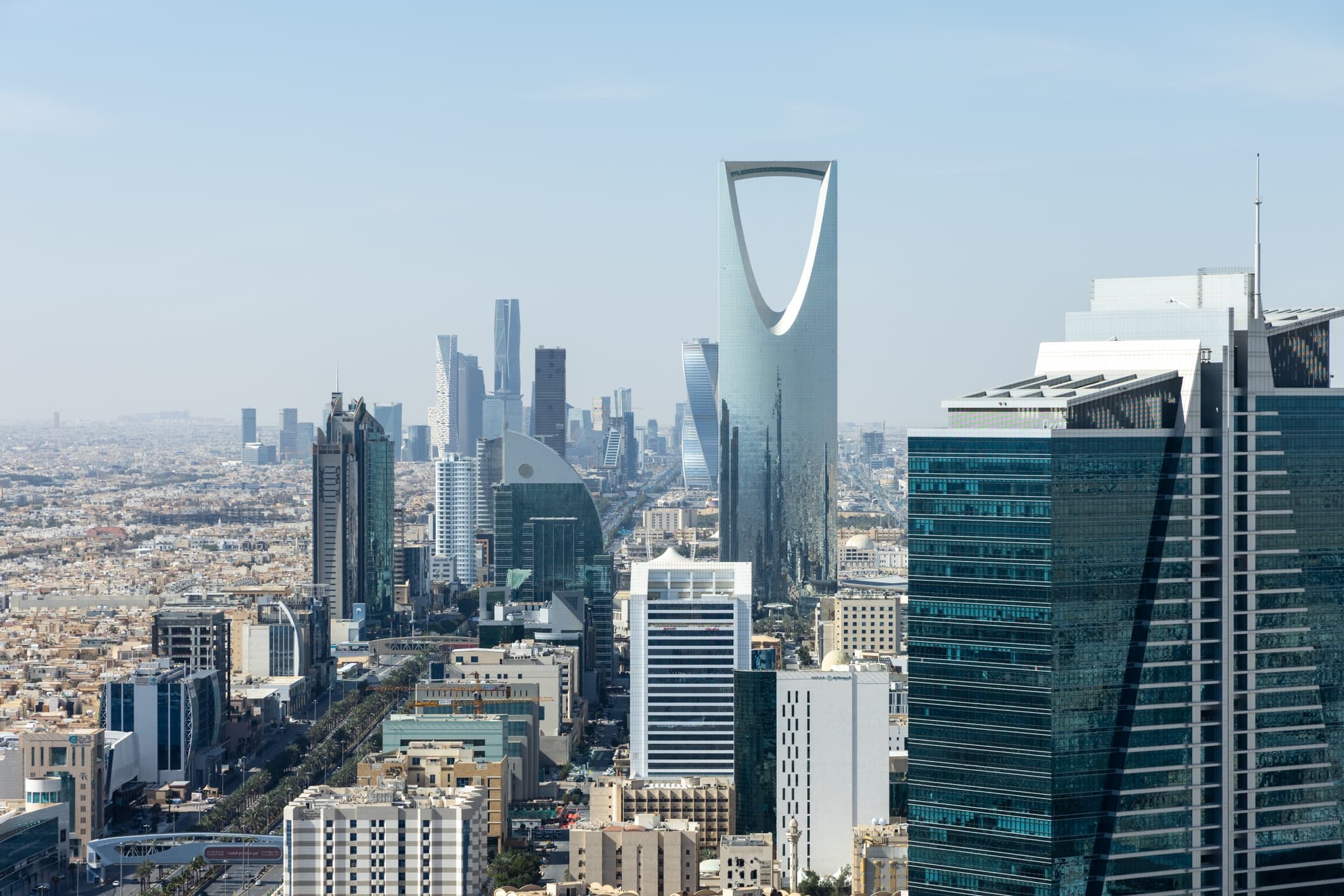 Dubai skyline featuring the tall glass-shaped tower with a curved cutout, surrounding modern high-rise buildings under a clear blue sky.