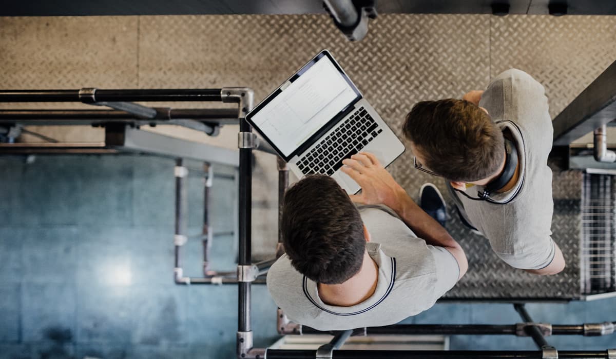 Top-down view of two people on a metal staircase, looking at an open laptop between them.