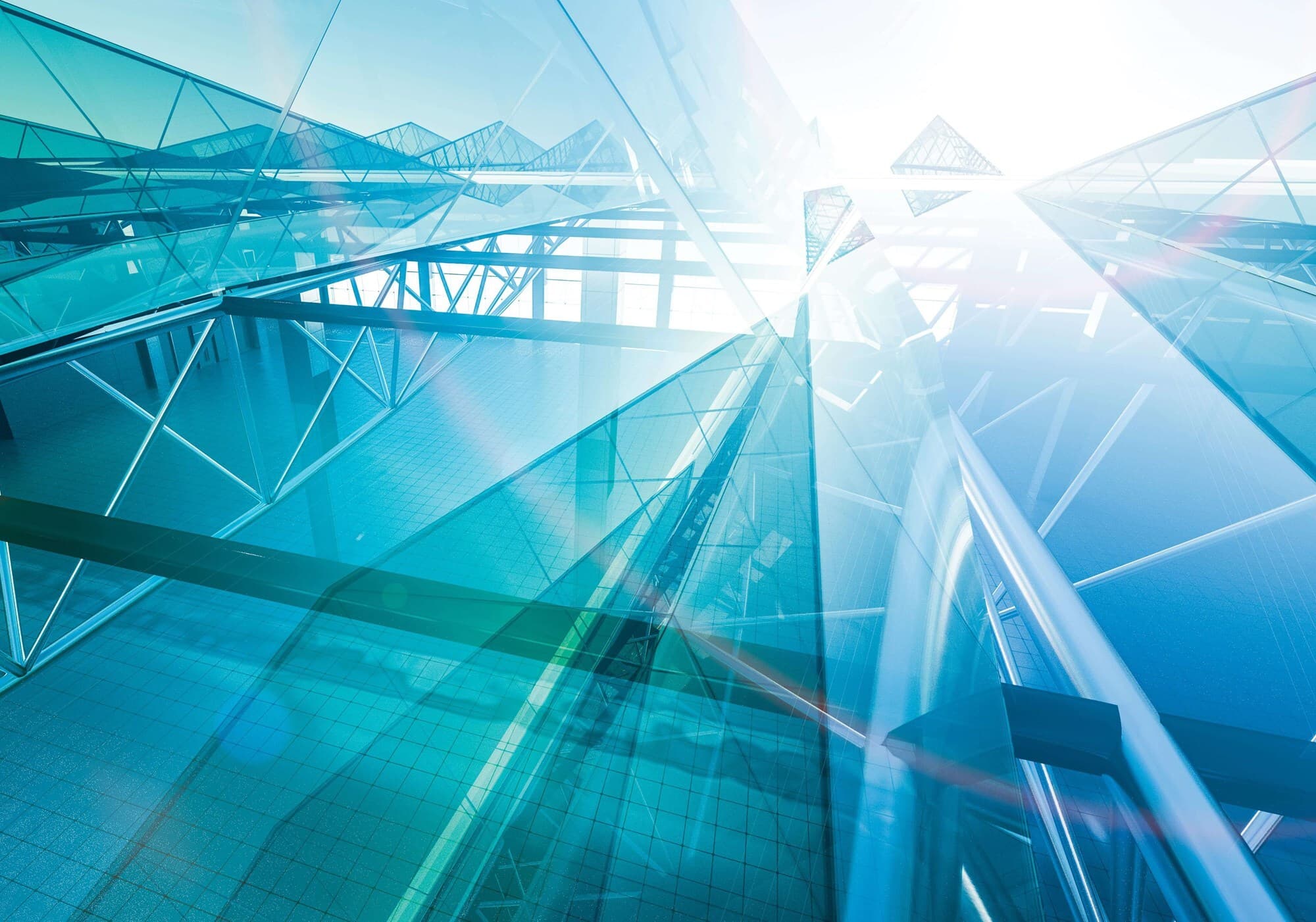 Futuristic interior of a glass building with blue-tinted translucent panels, metal framework, and intersecting beams, bathed in bright natural light.
