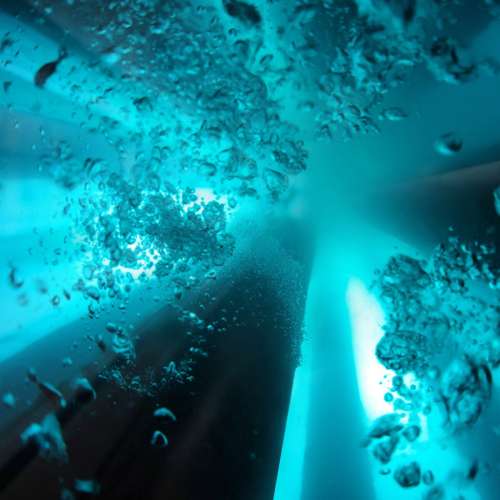 Underwater scene with teal lighting, numerous bubbles, and a dark curved form at the center amid floating particles.